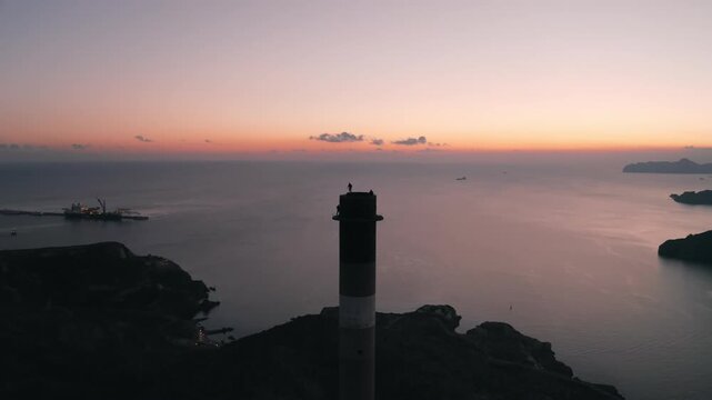Aerial top shot of 3 people standing on topo of an old abandoned chimney overlooking at some mountains and the sea at sunset in Cartagena, Spain Chimenea de Pe&ntilde;arroya