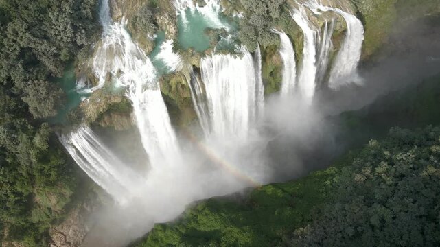 Drone bird's eye view of Tamul Waterfall with cascade and mist creating rainbow light arches