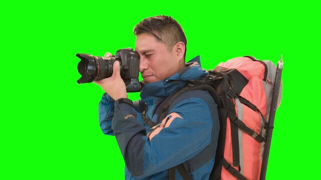 Adult man with backpack, posing in a studio with green screen, takes pictures with a camera. Concept travel and hiking.