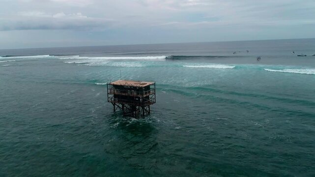 Judging tower structure looks out to waves at Cloudbreak Fiji with surfers, aerial dolly