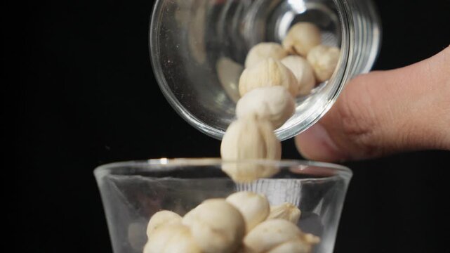 White Cardamom, Cardamon, or Cardamum (Amomum Cardamomum). Hand Pouring Round, Dry, Pods Into A Glass Cup In Slow Motion; Product Isolated On Black. 