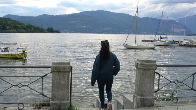 Woman Traveler Walking On The Pier Of Laveno Mombello In Varese, Italy. Tracking Shot