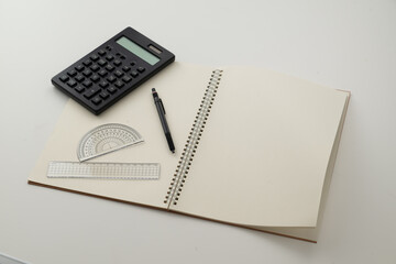 Collective image of stationery.
Notebook, protractor, ruler, calculator and pen.