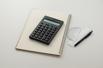 Collective image of stationery.
Notebook, protractor, ruler, calculator and pen.