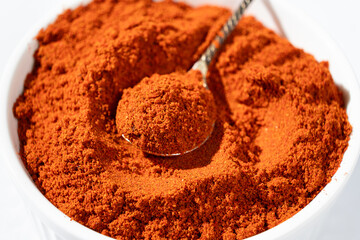 Ground smoked paprika in a spoon on a white background.