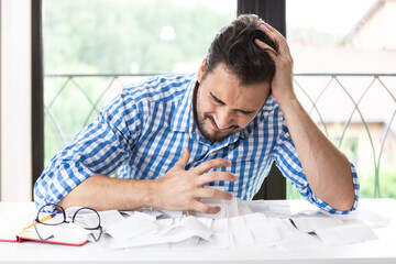 Close up of unhappy man sitting at the table, stressed and confused by calculate expense from...