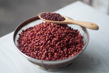 Azuki or Adzuki beans (Japanese red bean or red mung bean) after soaked in basket and dried in wooden spoon isolated on a table closed up. Selective focus blur background.