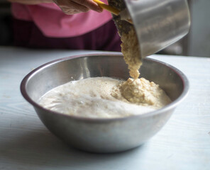 A woman is pouring grinded soybeans after soaking, process of making soymilk (soybean milk or hoya milk) isolated on table in kitchen closed up selective focus blur background.