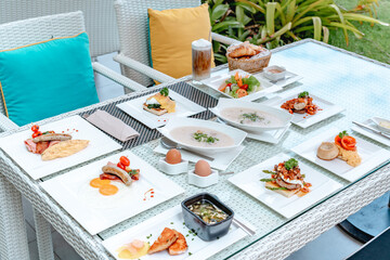 Breakfast in luxury hotel. Table full of various food from buffet in modern resort. Morning food - fresh bakery, glasses of orange juice, eggs, cold cuts and plate with tropical fruits in restaurant