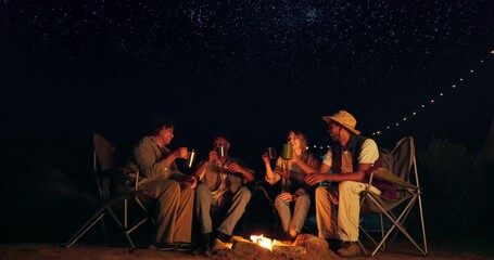 Camping, cheers and night with friends by fire outdoor in nature for adventure, bonding or getaway together. Travel, toast and dark with group of happy young people drinking on holiday or vacation