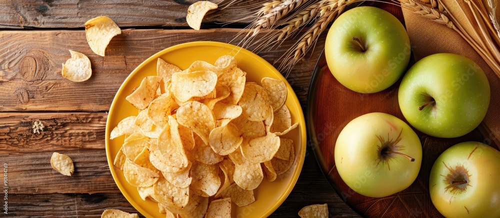 Poster top view of apple chips on a yellow plate surrounded by a green apple and wheat spica on a wooden ta