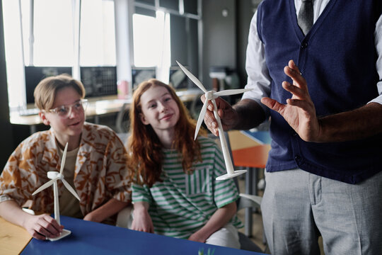 Selective focus shot of unrecognizable teacher holding wind turbine model telling teenagers about renewable energy