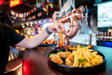 Close-up of a hand dipping a crispy fried chicken strip into a creamy sauce, with a side of golden...