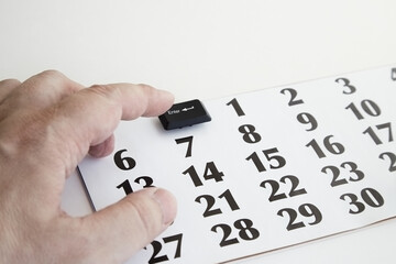 A hand presses the Enter key from a computer keyboard on a calendar instead of the first day of the...