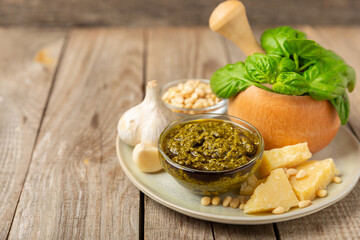 Pesto. Italian basil pesto sauce on a textured wooden background. Ingredient for pesto sauce: fresh basil, pine nuts, Parmesan cheese and olive oil. Space for text.Copy space.