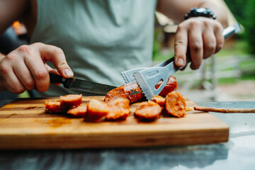 Close up of man hands cutting bbq sausage with knife