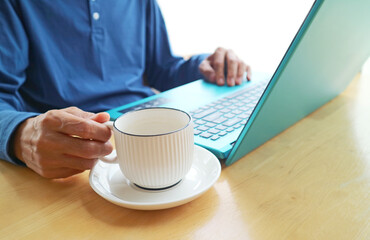 Closeup of hand holding a cup of coffee while working on laptop