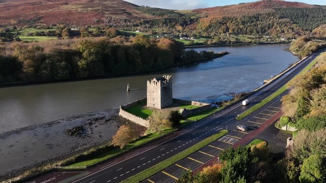 Narrow Water Castle, County Down, Northern Ireland, November 2022. Drone orbits Tower House counter clockwise on the banks of the Newry river with Autumn foliage on a warm sunny morning.