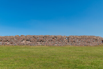 three stripes - green grass, a medieval castle wall made of stones and bricks, blue sky. © Ieva
