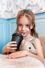 Cute little girl in blue dress drinking cocktail and sitting in cafe