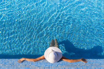 Brunette woman in white hat relaxing at the pool during vacation