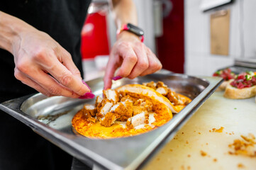 A close-up of hands preparing food, placing sliced grilled chicken on a dish with sauce. The image captures the action of cooking, emphasizing fresh ingredients and culinary skill.