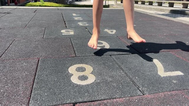 Child playing barefoot on numbered hopscotch tiles at an outdoor playground