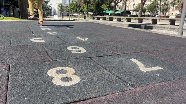 Child girl playing barefoot on numbered hopscotch tiles at an outdoor playground