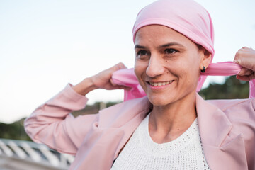 Woman with cancer putting on the pink scarf to demonstrate her fight against the disease. Concept:...