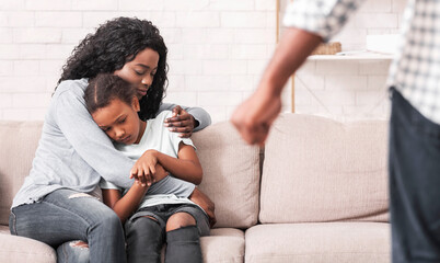 Victims of domestic violence. Afro mother and daughter suffering from home abuse, sitting on couch...