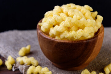Cheese corn sticks in wooden bowl on dark wooden background.