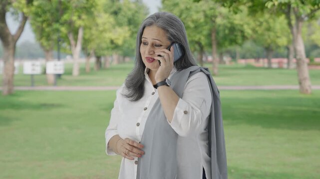 Happy Indian mother talking on phone in park
