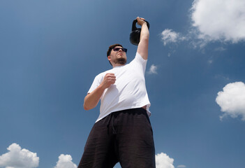 Sportive man workout with kettlebell outdoor in spring or summer