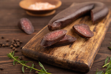 Sujuk sausage on wooden cutting board with pepper and herbs on brown wooden. Side view, selective focus