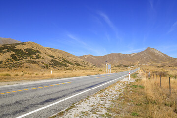 Lindis Pass, an unusual view with tussocks cover mountain. The color blue sky contrasts with the yellow of grassland.