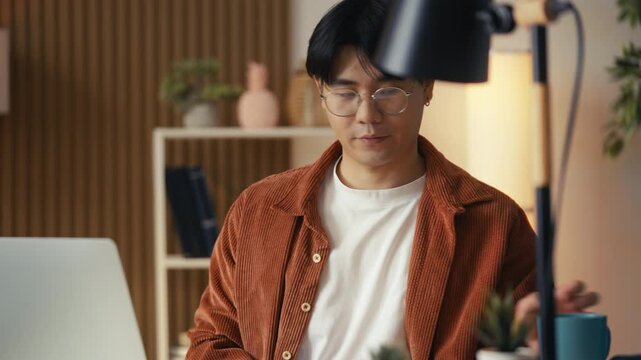Asian man freelancer opening laptop and drinking coffee, beginning of work day