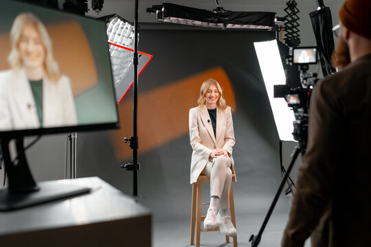 Woman in casual outfit sitting in professional video recording studio with camera and lights