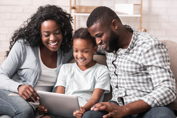 Cheerful black family using digital tablet together at home, watching funny videos.