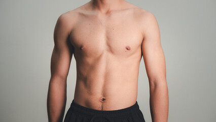 Fototapeta premium Handsome muscular young man posing against a grey background. male model taking off his shirt on a gray background, body transformation , weight loss, sixpack