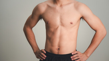 Obraz premium Handsome muscular young man posing against a grey background. male model taking off his shirt on a gray background, body transformation , weight loss, sixpack