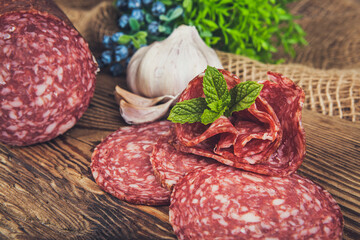 Sliced salami with garlic and herbs on a wooden background