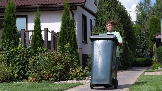 boy drags green trash can from a private home. kid does chores