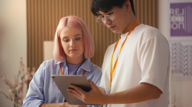 Female web developer and her Asian colleague discussing new program on tablet