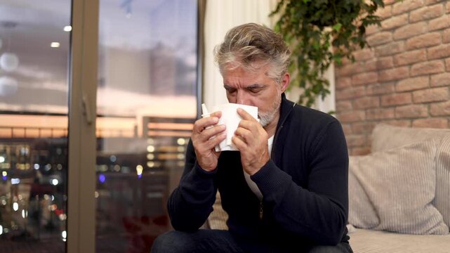 Senior man sitting at home and using a nose spray for his allergy