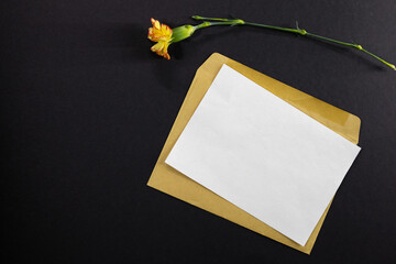 Top view of a kraft paper envelope, overflowing with bright yellow carnation flowers on a black background.