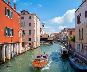 Venice, Italy - June 05, 2024: Man crossing canal on the orange boat.