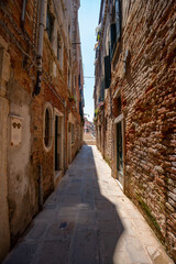 Fototapeta premium Venice, Italy - June 05, 2024: Narrow empty street framed with brick buildings.