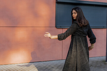 Happy positive dancer curling in dance. Woman with long dark dancing on urban street, on pink wall...