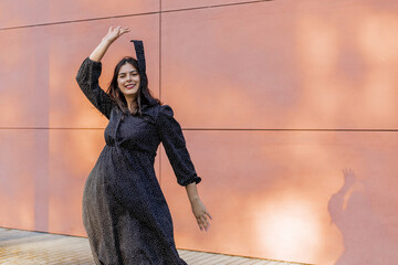 Happy positive dancer curling in dance. Woman with long dark dancing on urban street, on pink wall...