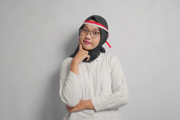 A woman wearing a white shirt and a black hijab with a red and white headband, looking thoughtful.